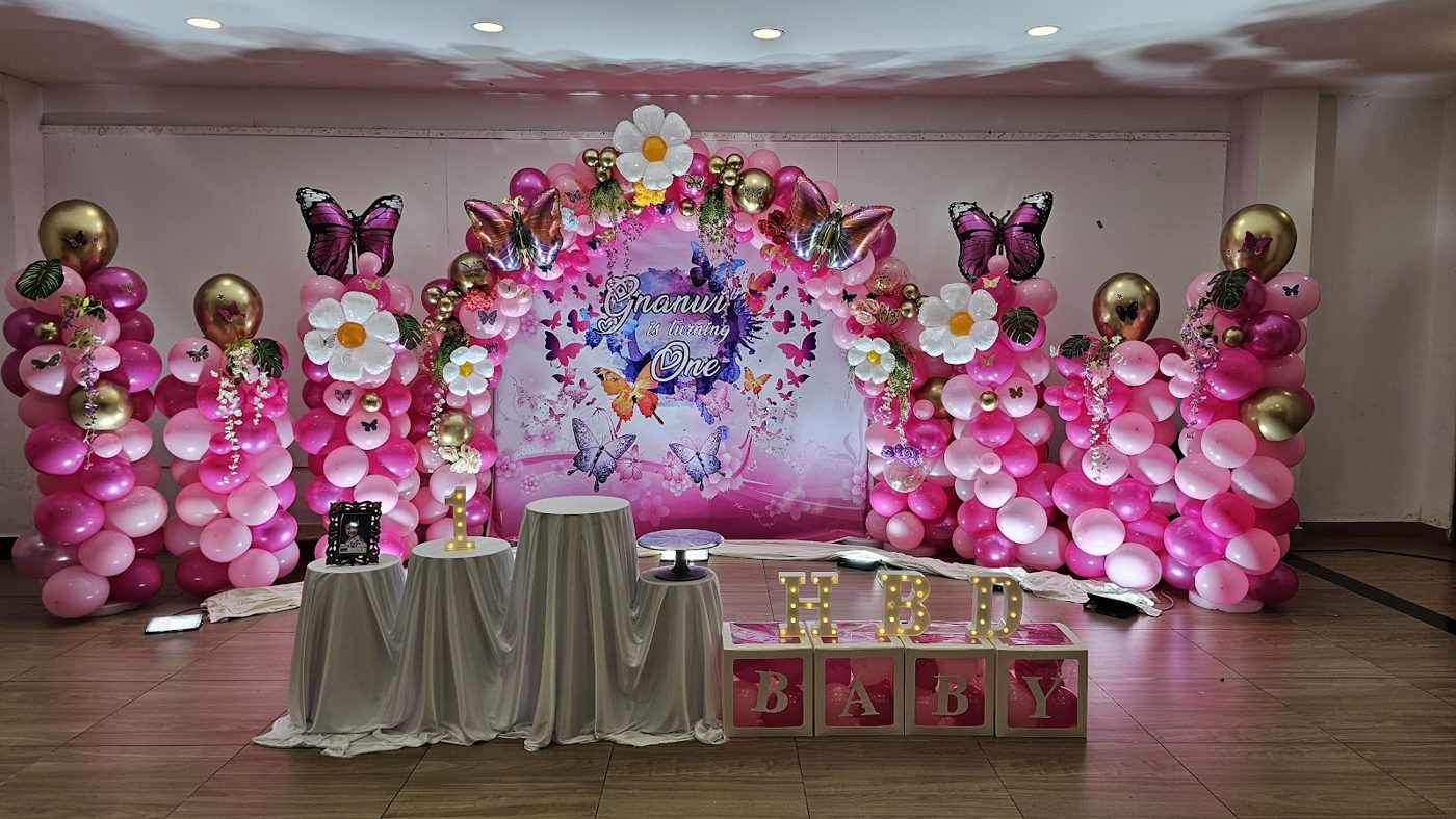 Pink butterfly 1st birthday setup with balloon arch and BABY boxes